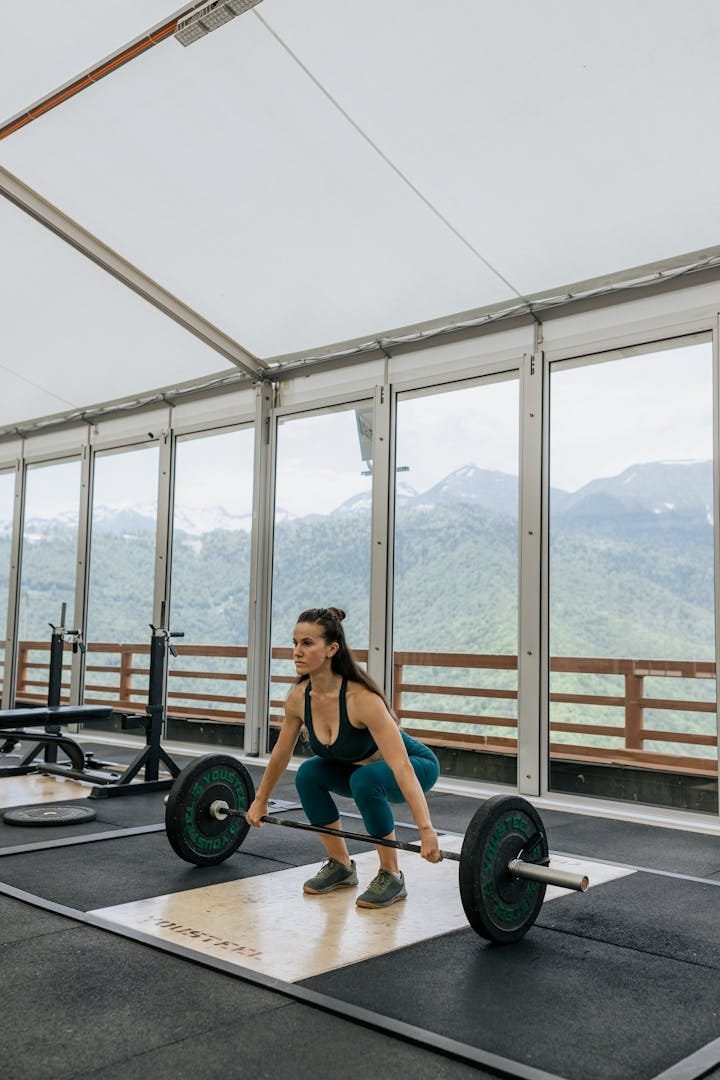 Photo by Anastasia Shuraeva Woman weightlifter exercising in a scenic gym with mountain views. Strength and focus.